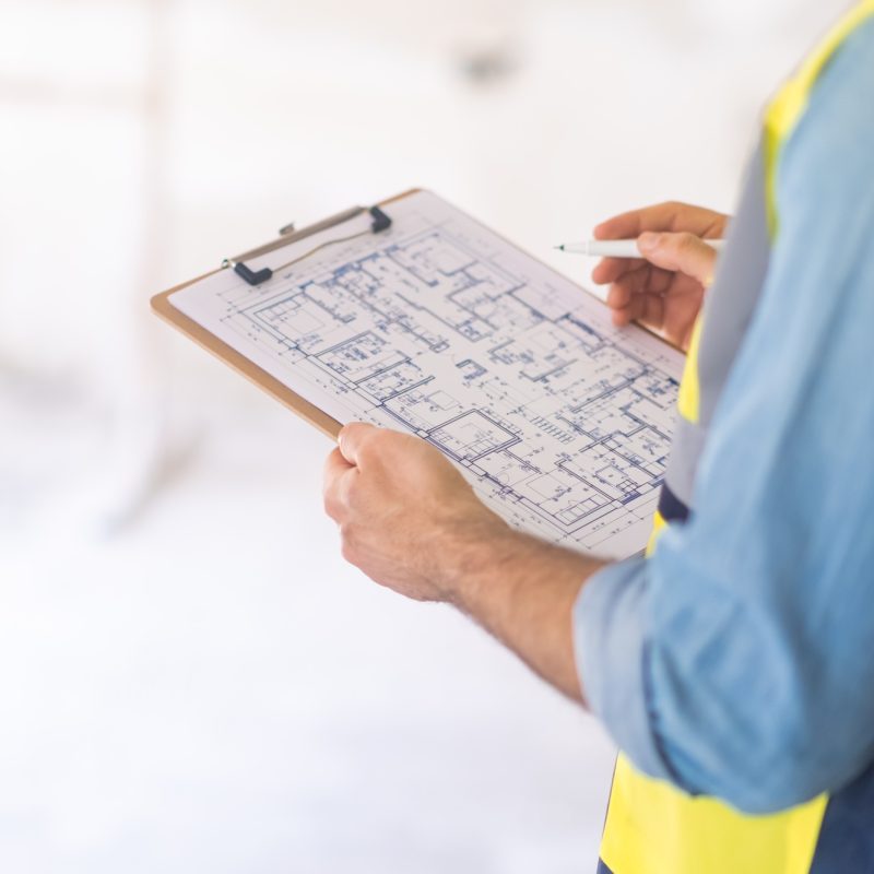Engineer examining construction documentation holding clipboard and pen in hands